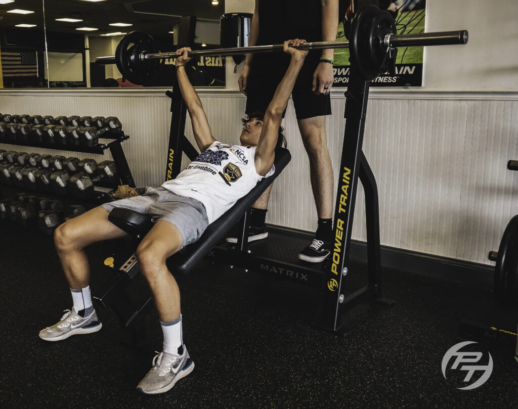 This is a young boy bench pressing with a trainer spotting him.